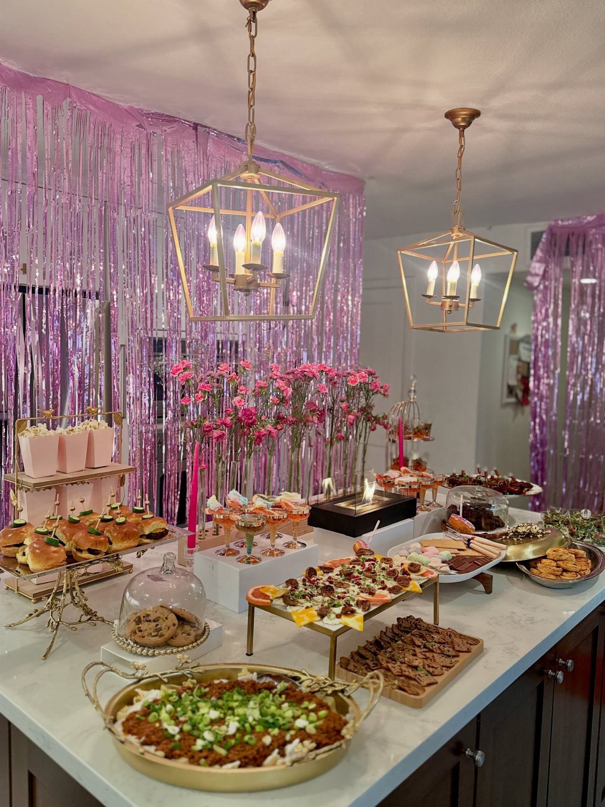 Buffet of appetizers and sweets on a counter with pink tinsel background.