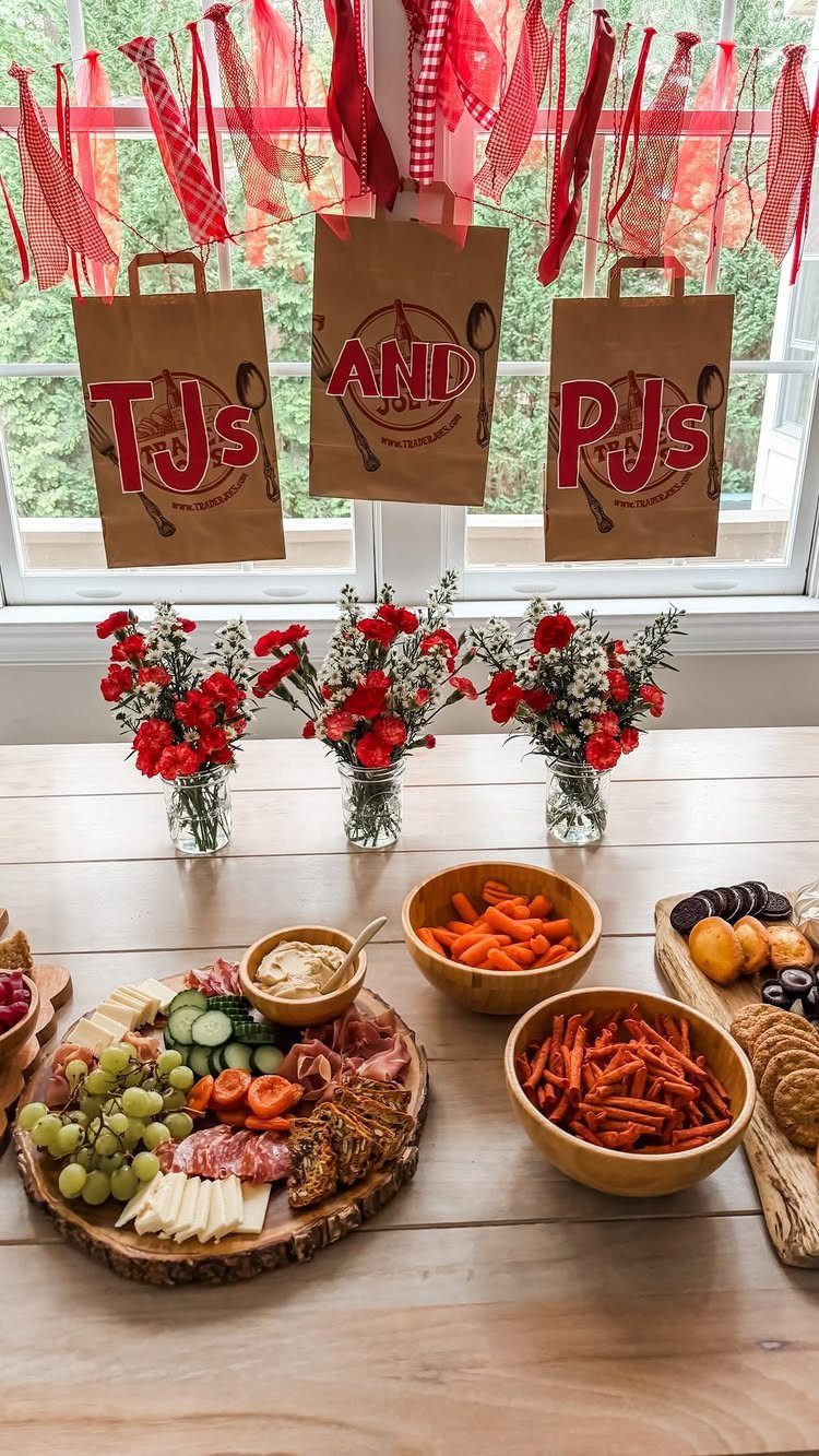 Party table with charcuterie, red flowers, and bags labeled TJs and PJs.