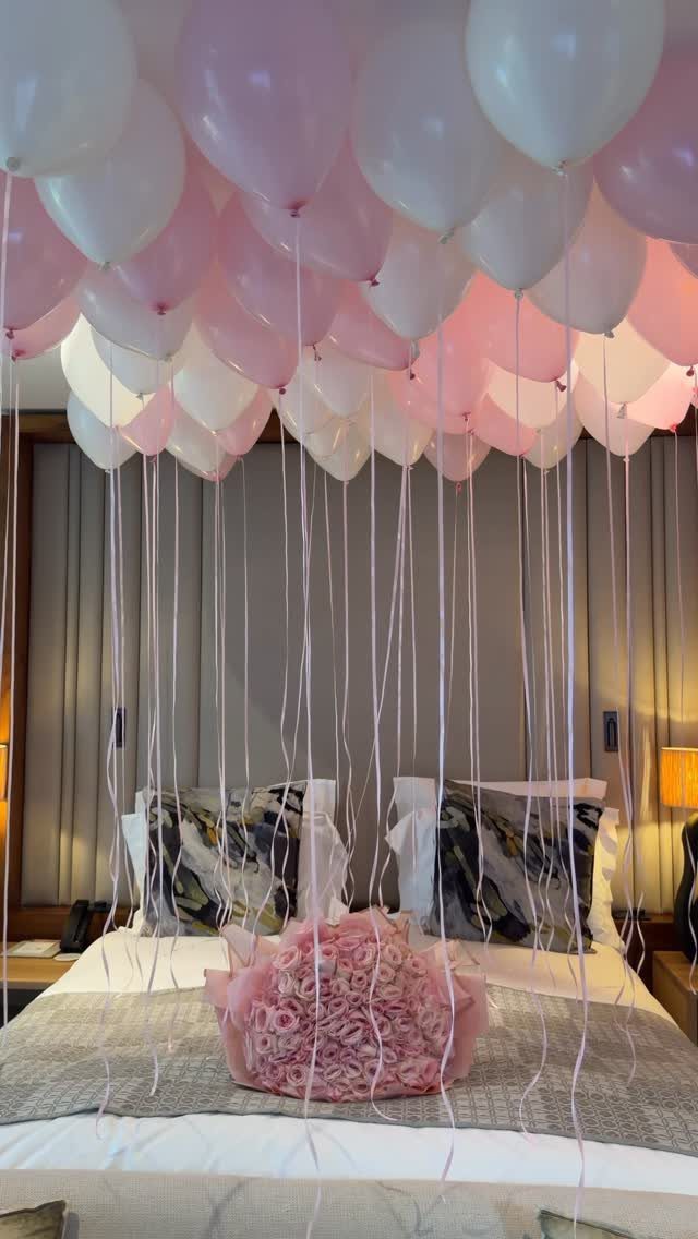 Hotel room bed with pink roses and pink and white balloons on ceiling