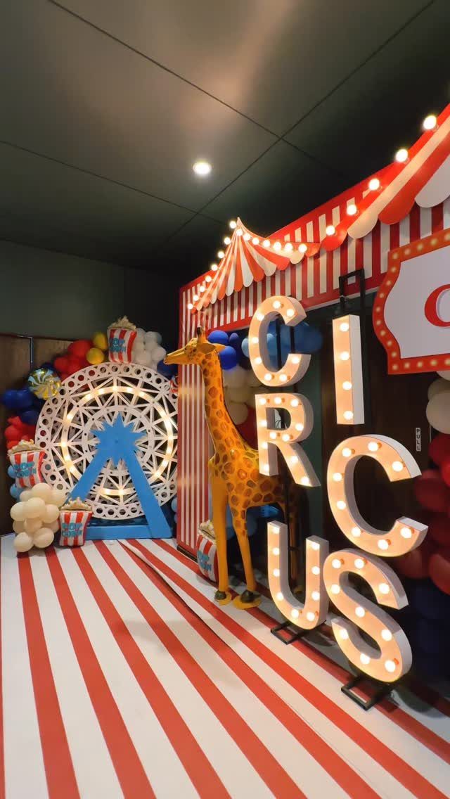 Circus-themed party venue with red striped floors, large glowing letters, and a giraffe statue.