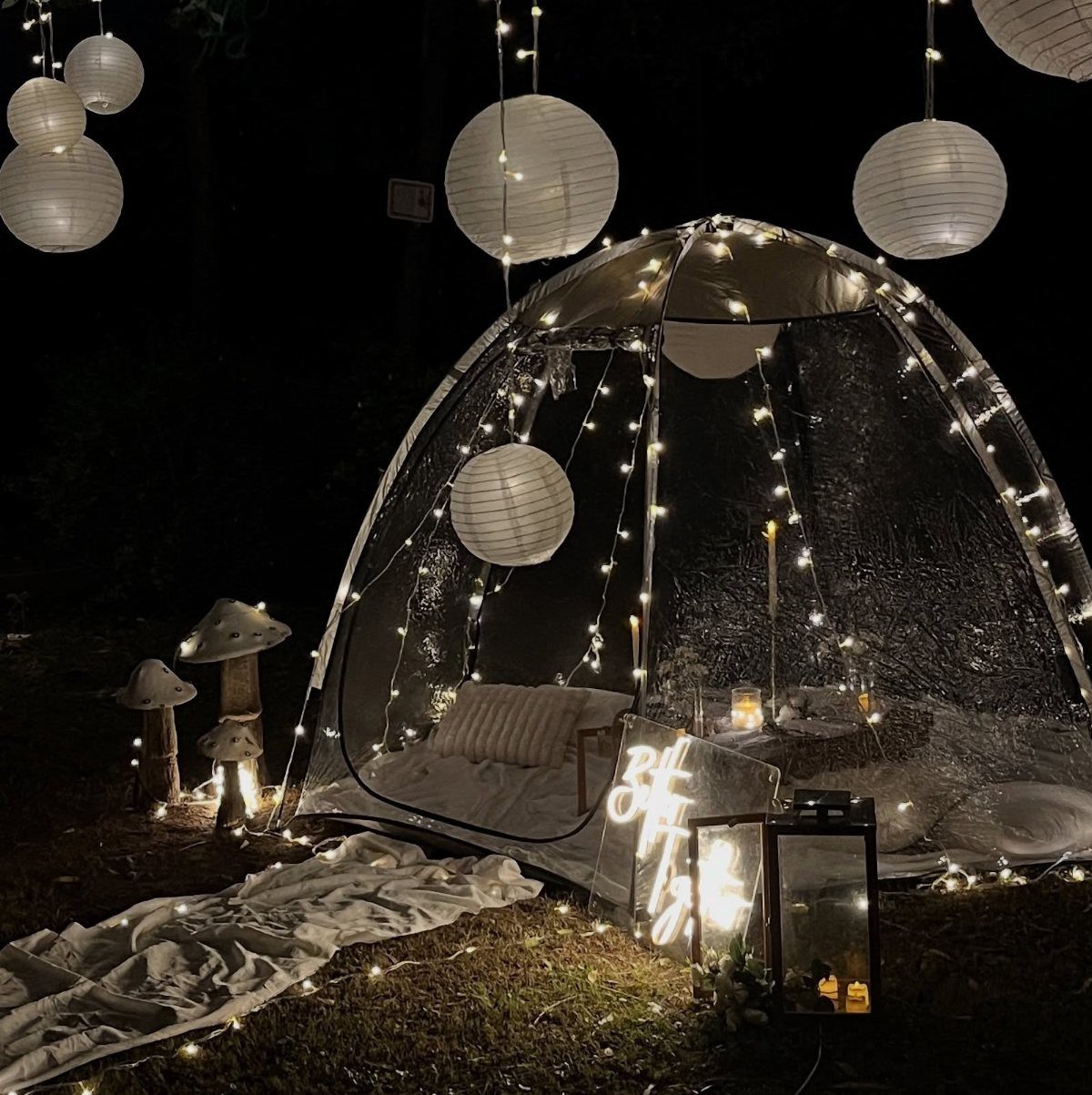 Transparent dome tent decorated with fairy lights and lanterns for a nighttime celebration.