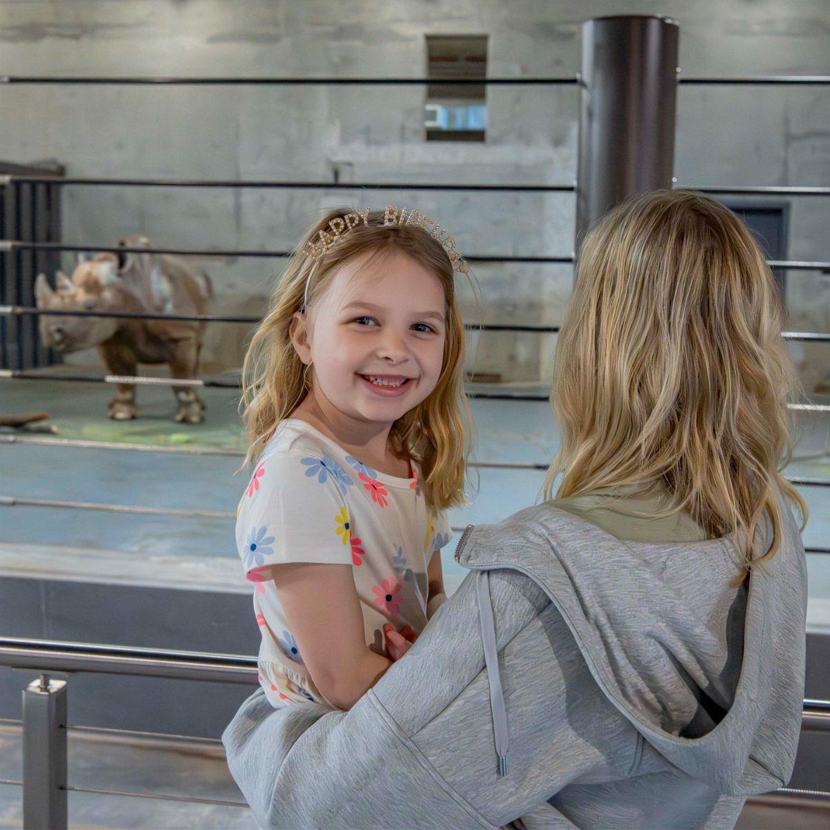 Smiling girl in birthday headband being hugged at a zoo with a rhino.