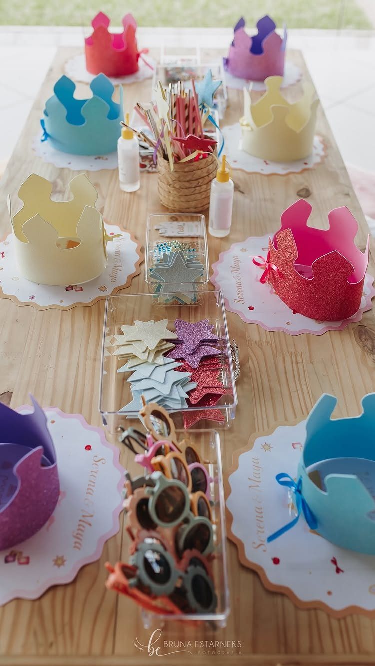Colorful glittery paper crowns and craft supplies arranged on a wooden table.