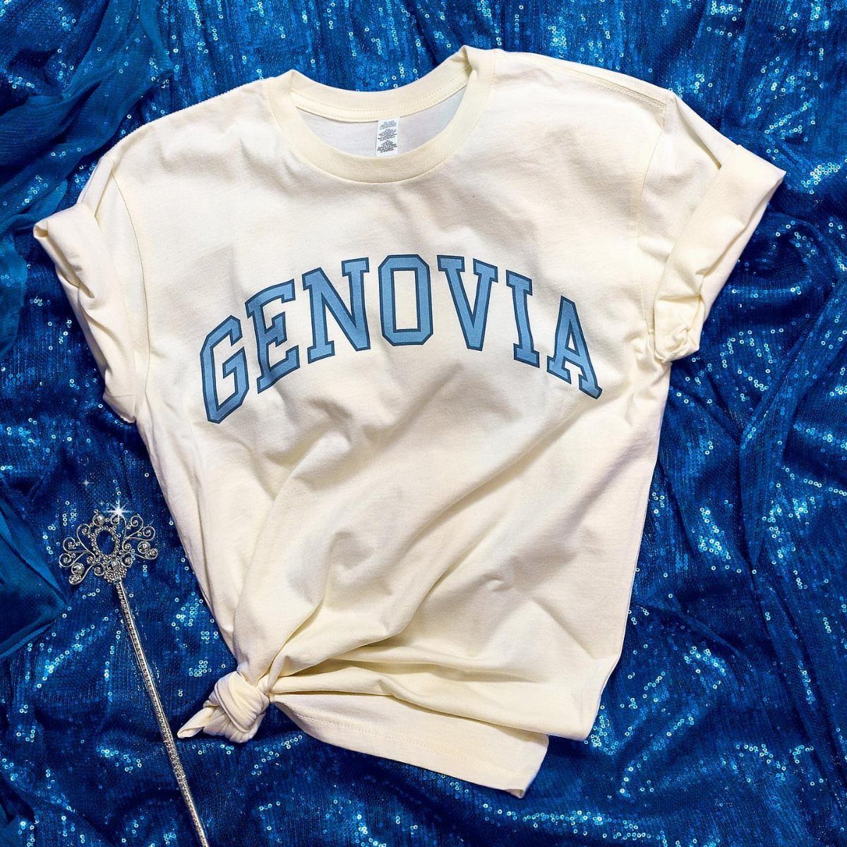 Cream t-shirt with blue Genovia text on blue sequins with a silver wand.
