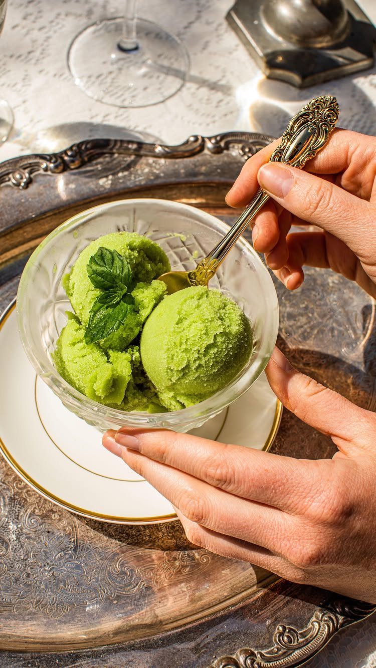 Green sorbet in a glass bowl held by hands over a silver tray