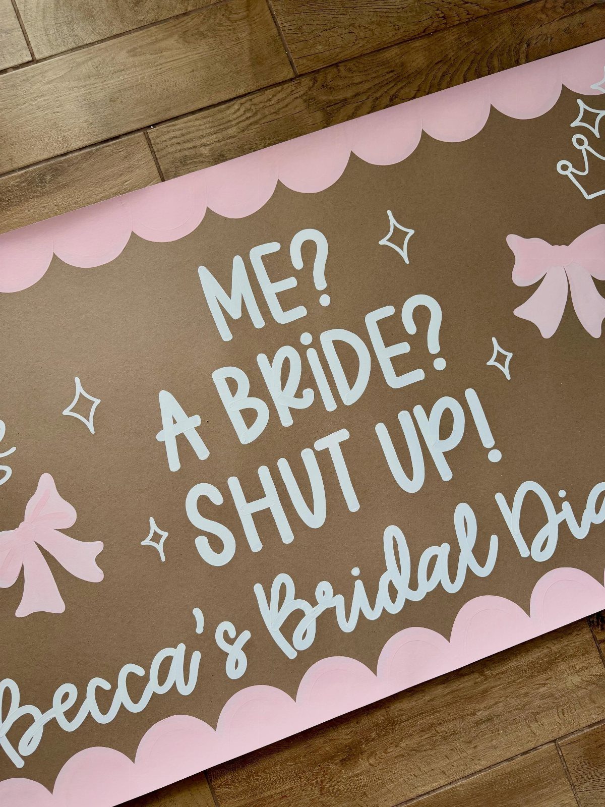 Brown bridal shower sign with pink scalloped edges and white hand-lettered text.