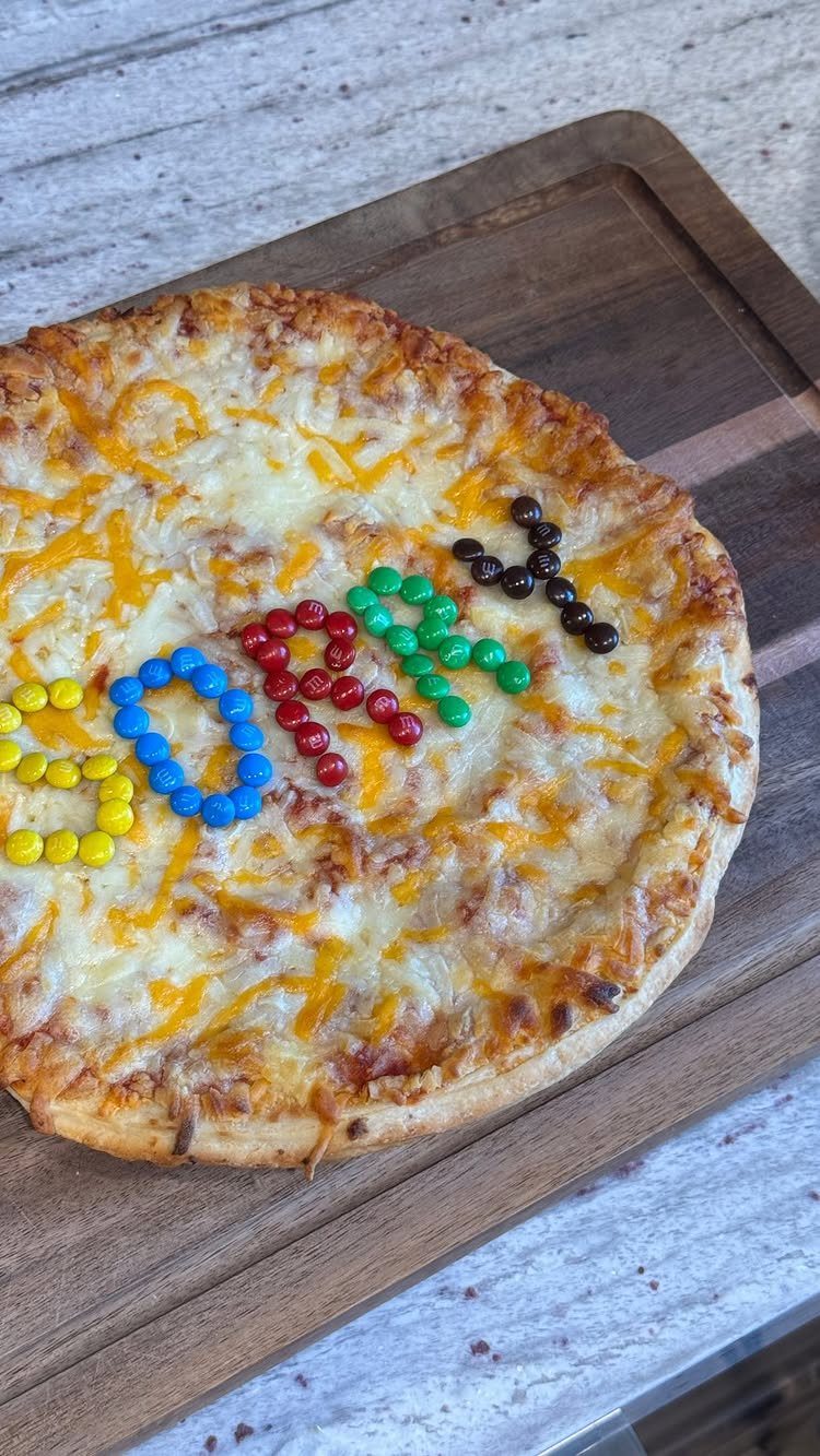 Cheese pizza on a wooden board with SORRY spelled in colorful candies.