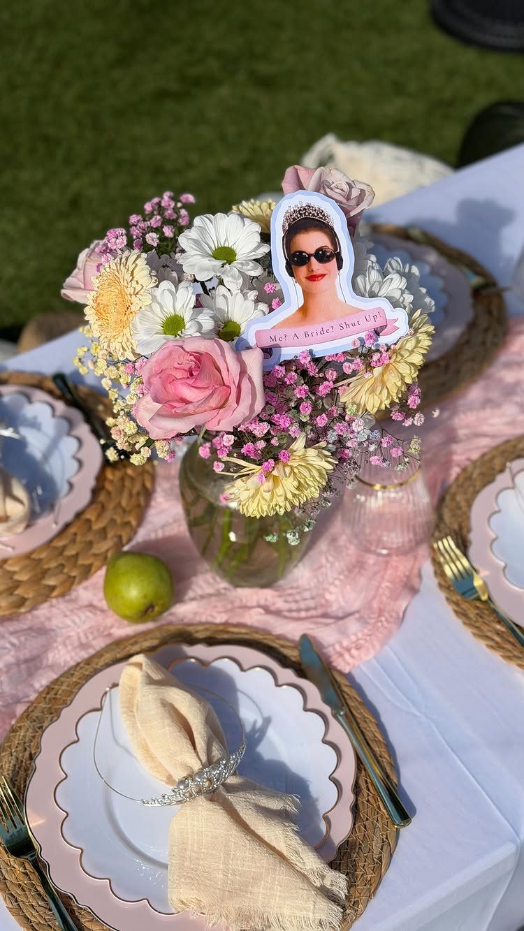 Table setting with pink plates, floral centerpiece, and a royal-themed cutout decoration.