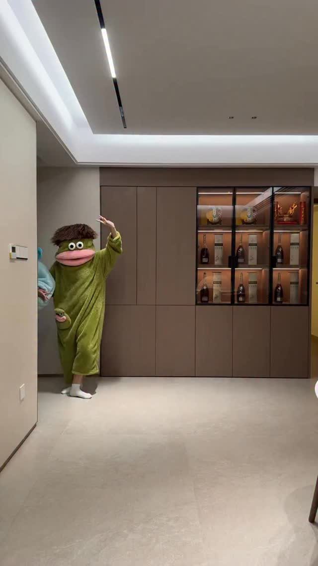 Person in a green frog onesie posing in a modern beige room.