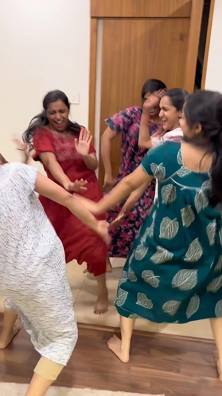 Women in colorful pajamas dancing and laughing together in a living room.