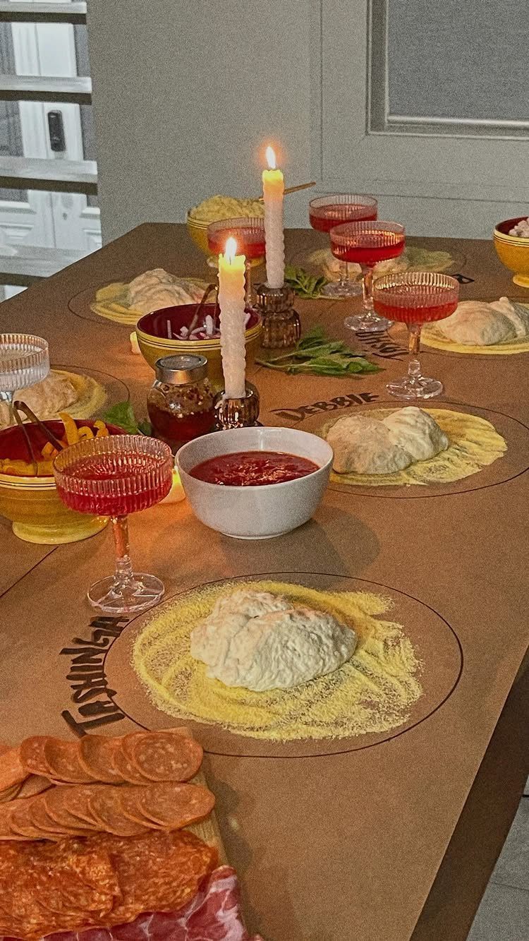 Pizza dough portions and toppings arranged on a table with red drinks and candles.