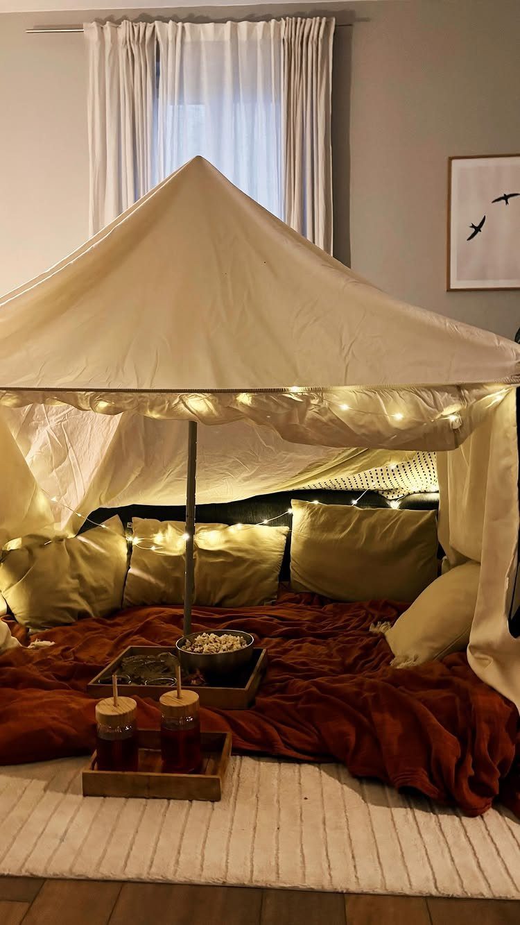 Indoor tent setup with warm string lights, green pillows, and snacks on trays.