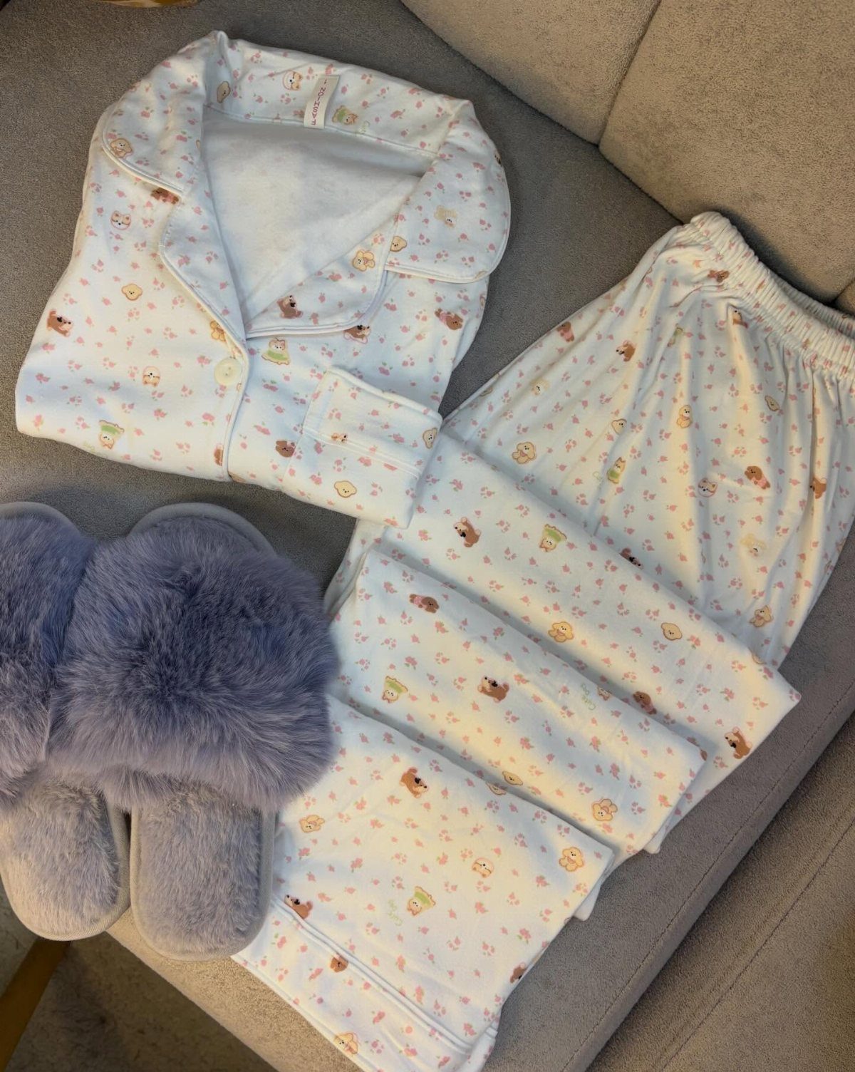 White patterned pajama set with fluffy purple slippers on a beige sofa.