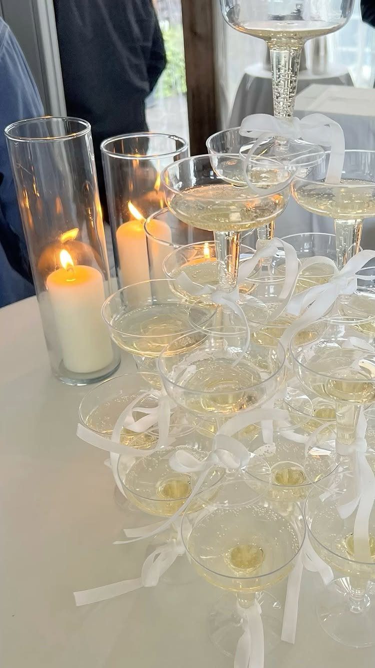 Champagne coupe glasses with white ribbons and lit candles on a white table.