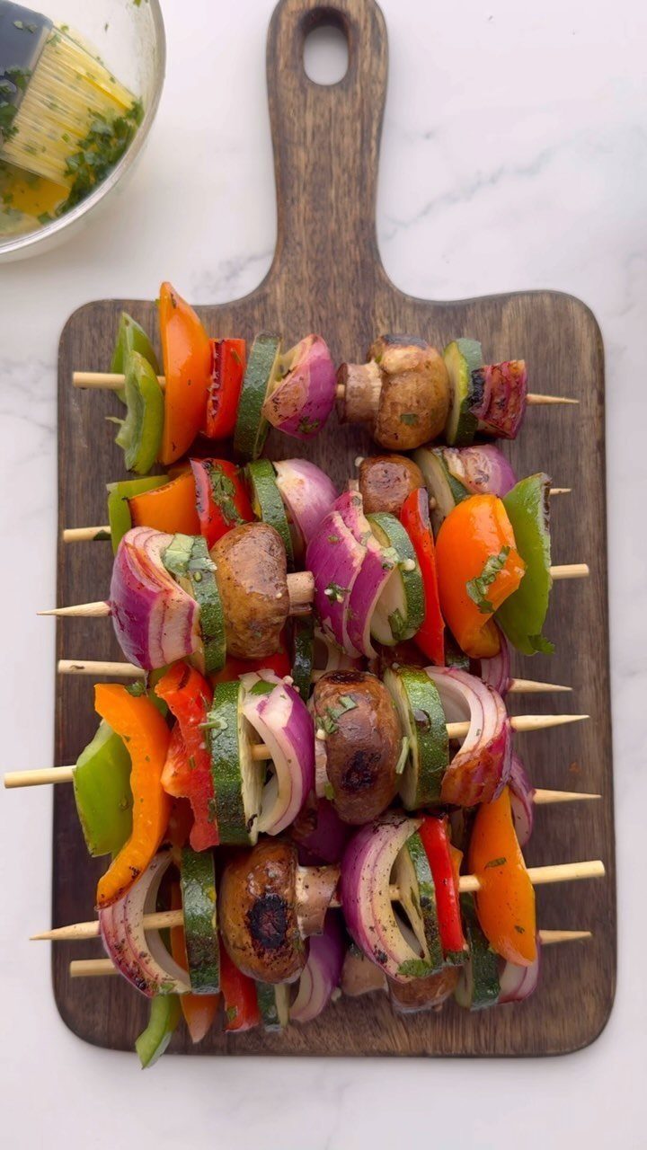 Grilled vegetable skewers with colorful peppers, onions, and zucchini on a wooden board.
