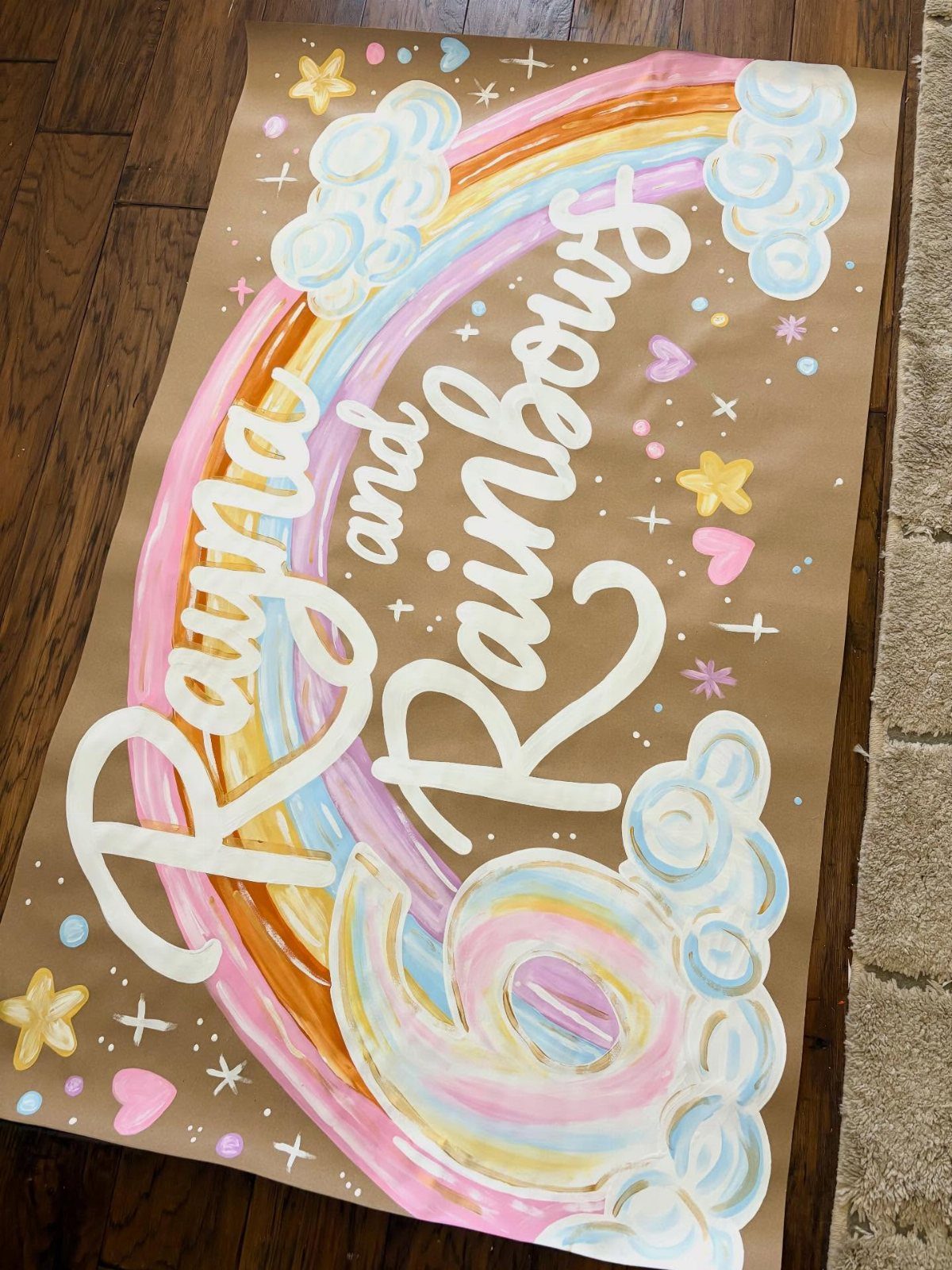Hand-painted rainbow banner on brown paper with white text and colorful stars.