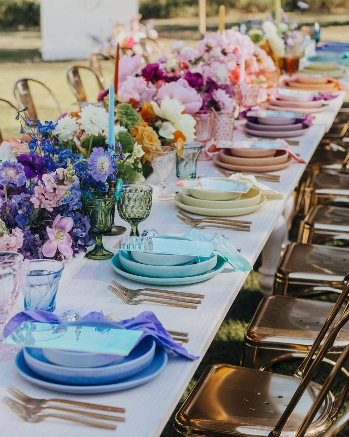 Colorful plates and glasses in rainbow hues set on a white outdoor table.