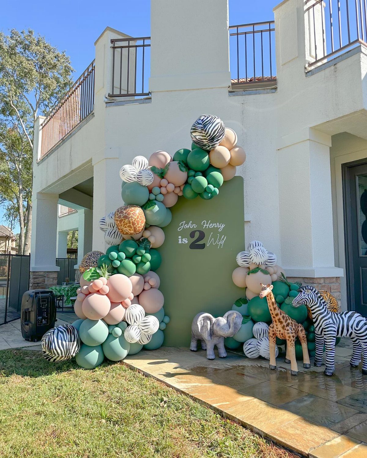 Animal themed second birthday backdrop with green balloons and inflatable safari animals.