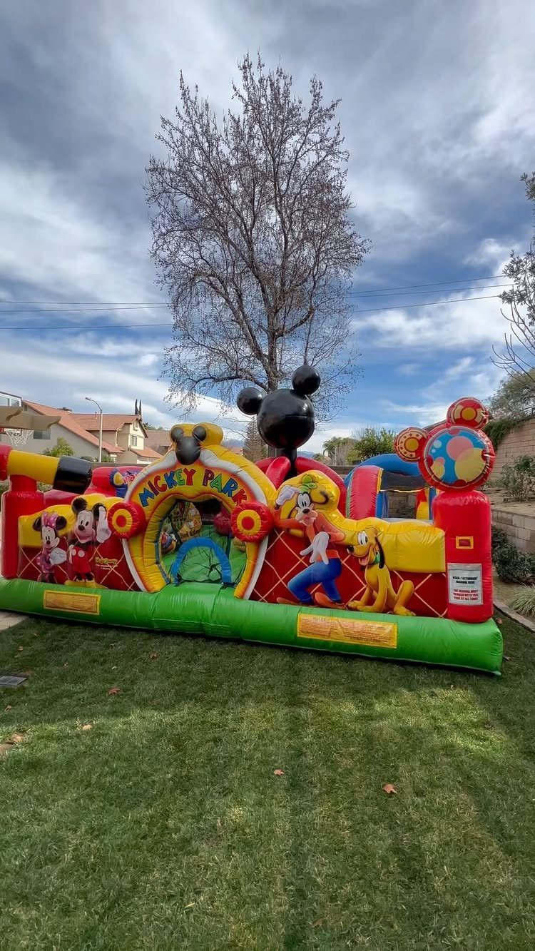 Colorful Mickey Mouse themed inflatable bounce house set up on a green grass lawn.