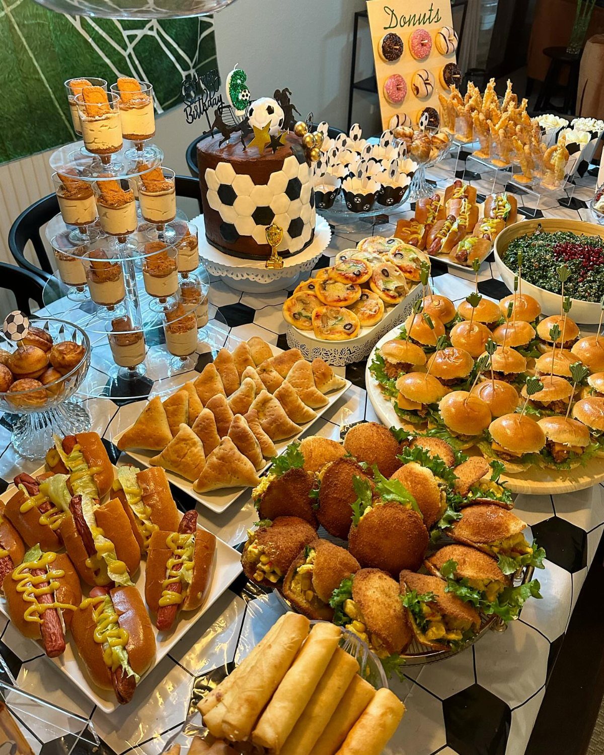 Soccer themed party food spread with a cake, sliders, and various appetizers.