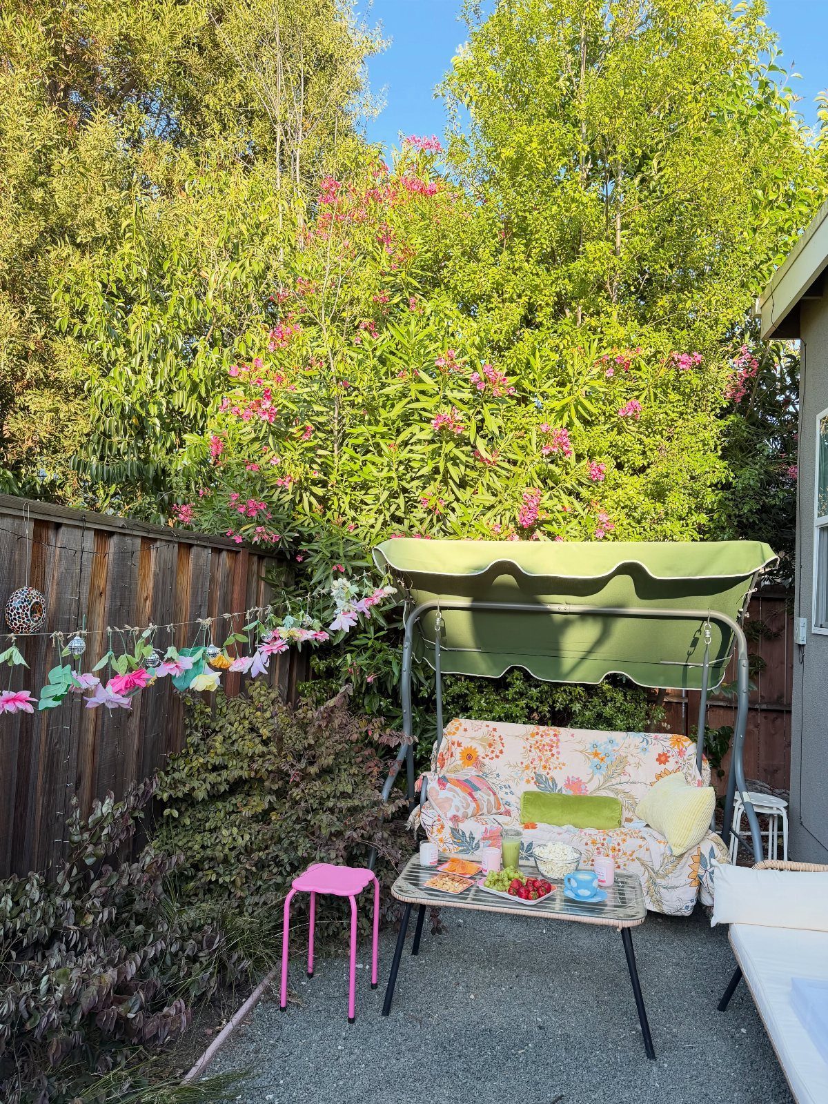 Outdoor patio setup with a cozy swing seat, snacks, and lush garden greenery.