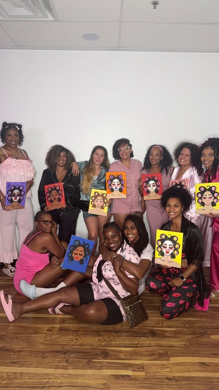 Group of women in pajamas holding identical colorful portrait paintings in a room.