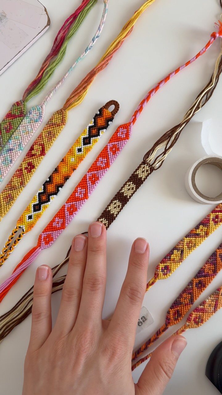 Hand resting beside several colorful, intricately woven handmade friendship bracelets on white surface.