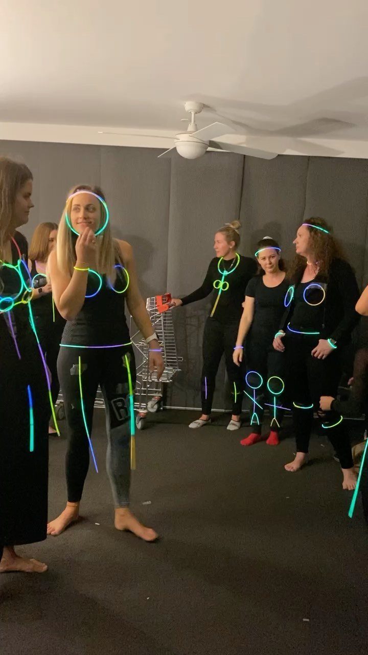 Women in black clothing wearing neon glow sticks in a dimly lit room.