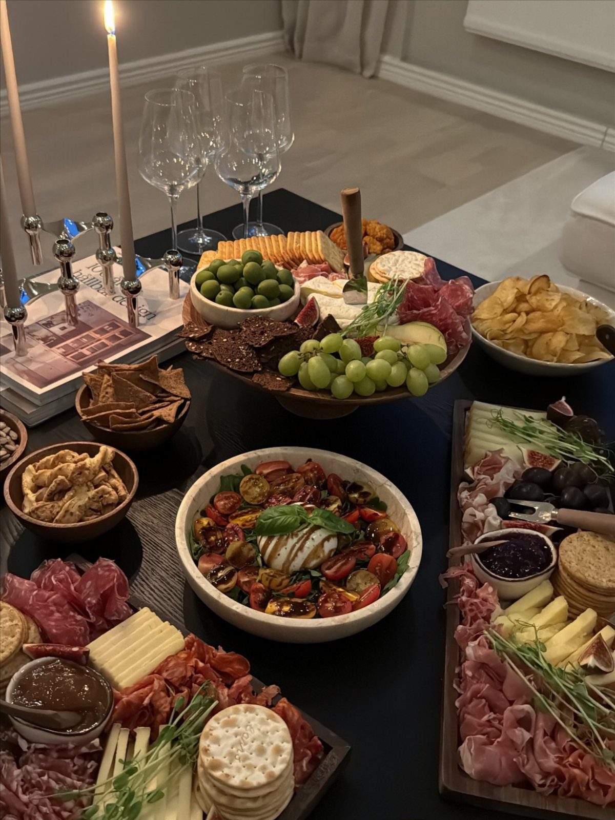 Charcuterie boards and appetizers with wine glasses and candles on a dark table.