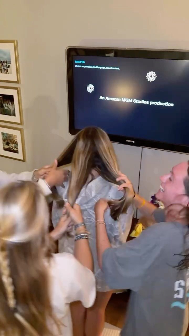 Three young women together in a room with a movie playing on TV.