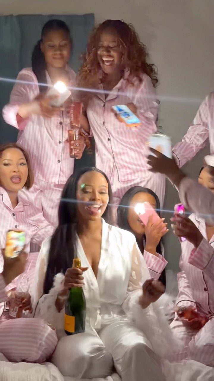 Women in pajamas laughing and holding champagne and phones during a sleepover party.