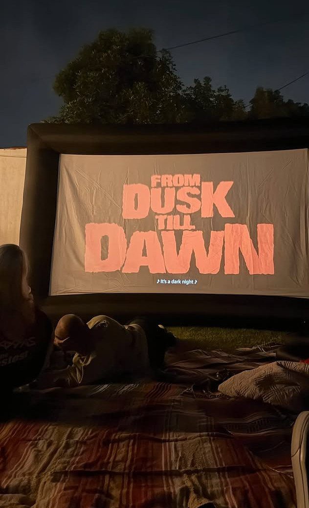 Outdoor movie screen showing a film title with people lounging on blankets.