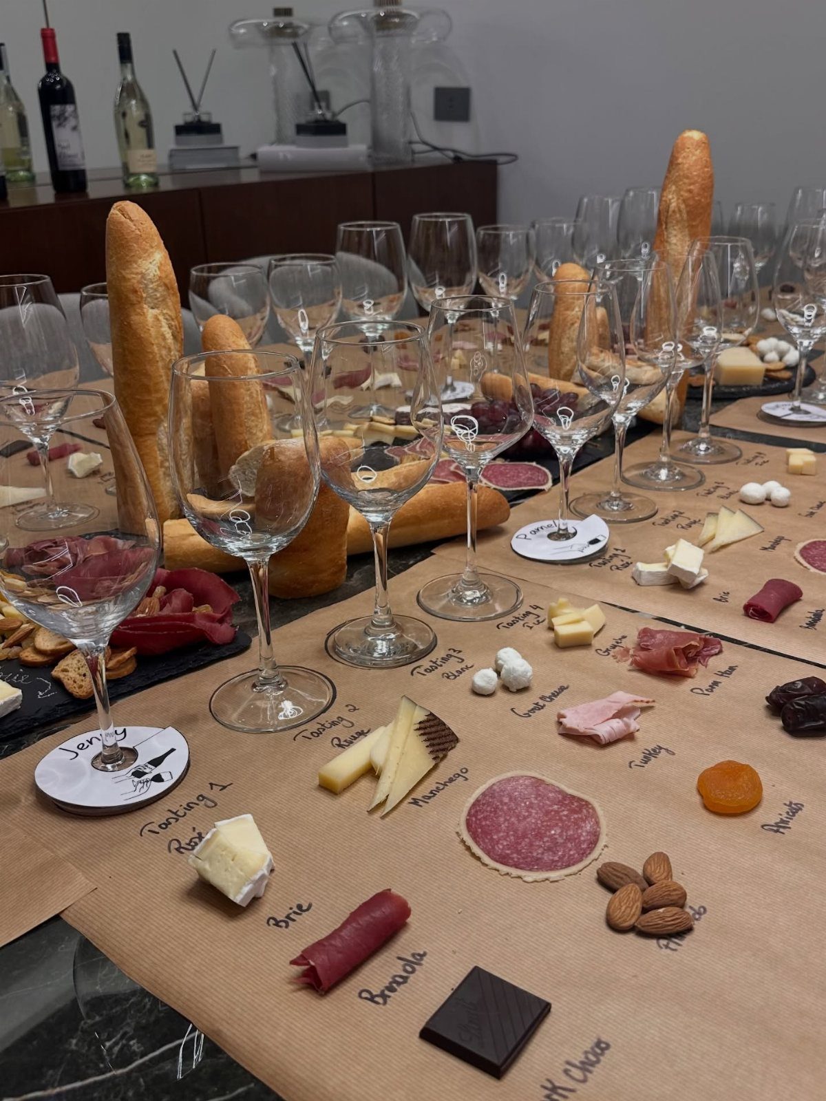 Wine tasting spread with glasses, baguettes, cheeses, and meats on brown paper.