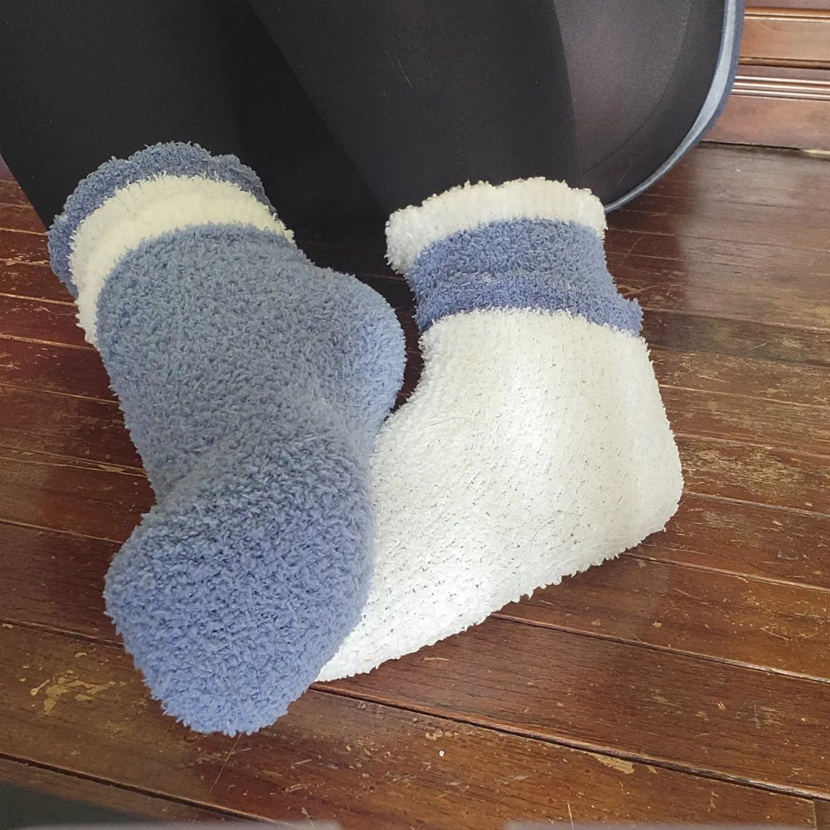 Fuzzy blue and white striped socks worn on a wooden floor.