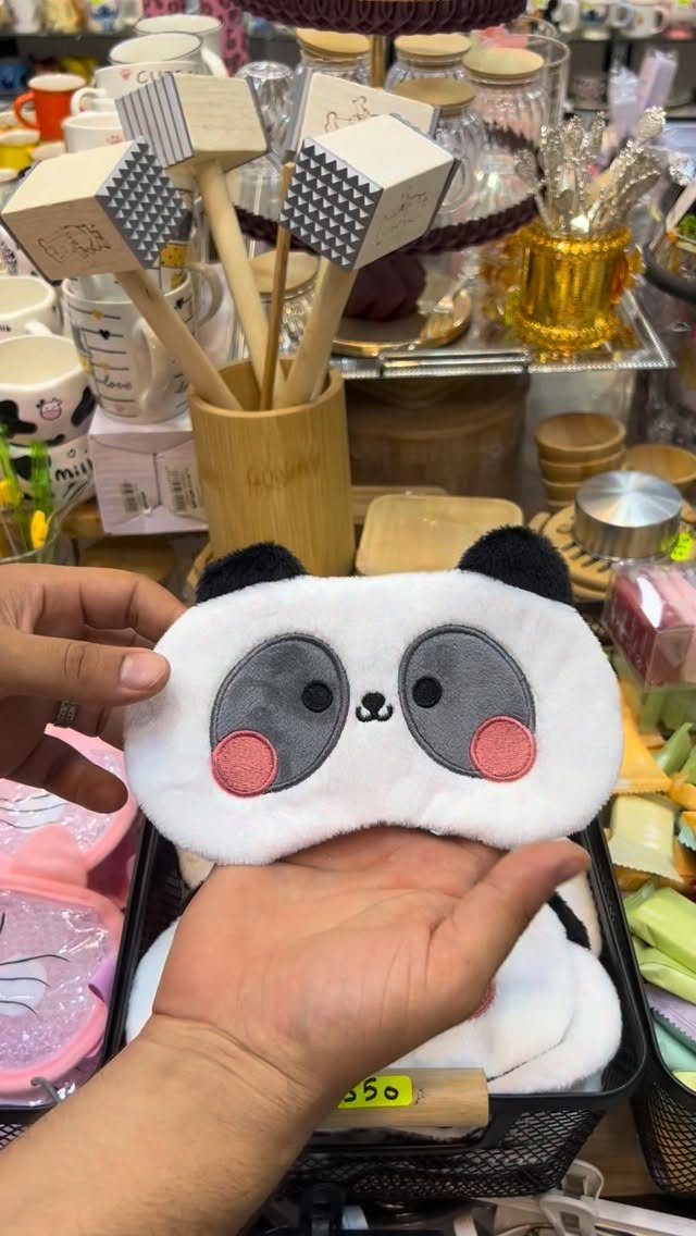 Panda themed plush sleep mask held in hands in a gift shop.