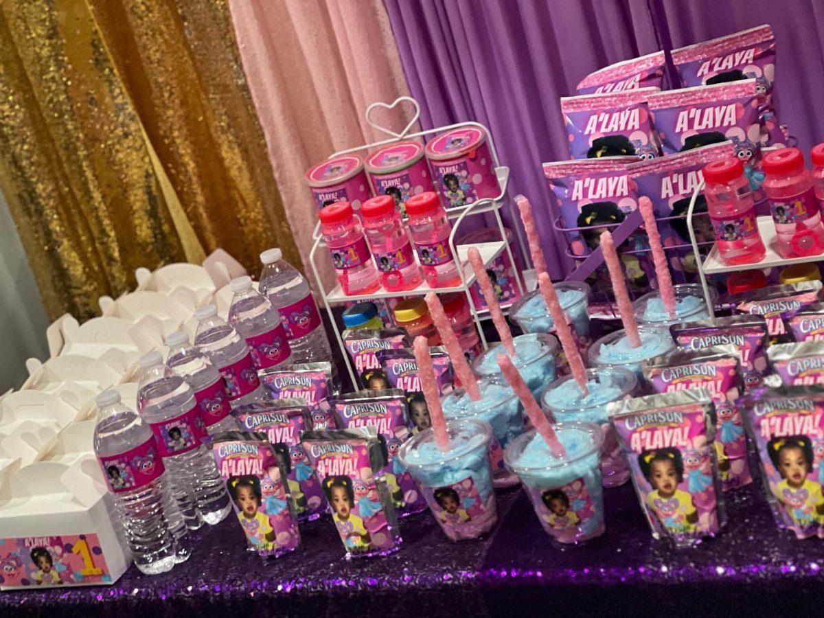 Personalized party favors including water bottles and juice pouches on a purple table.