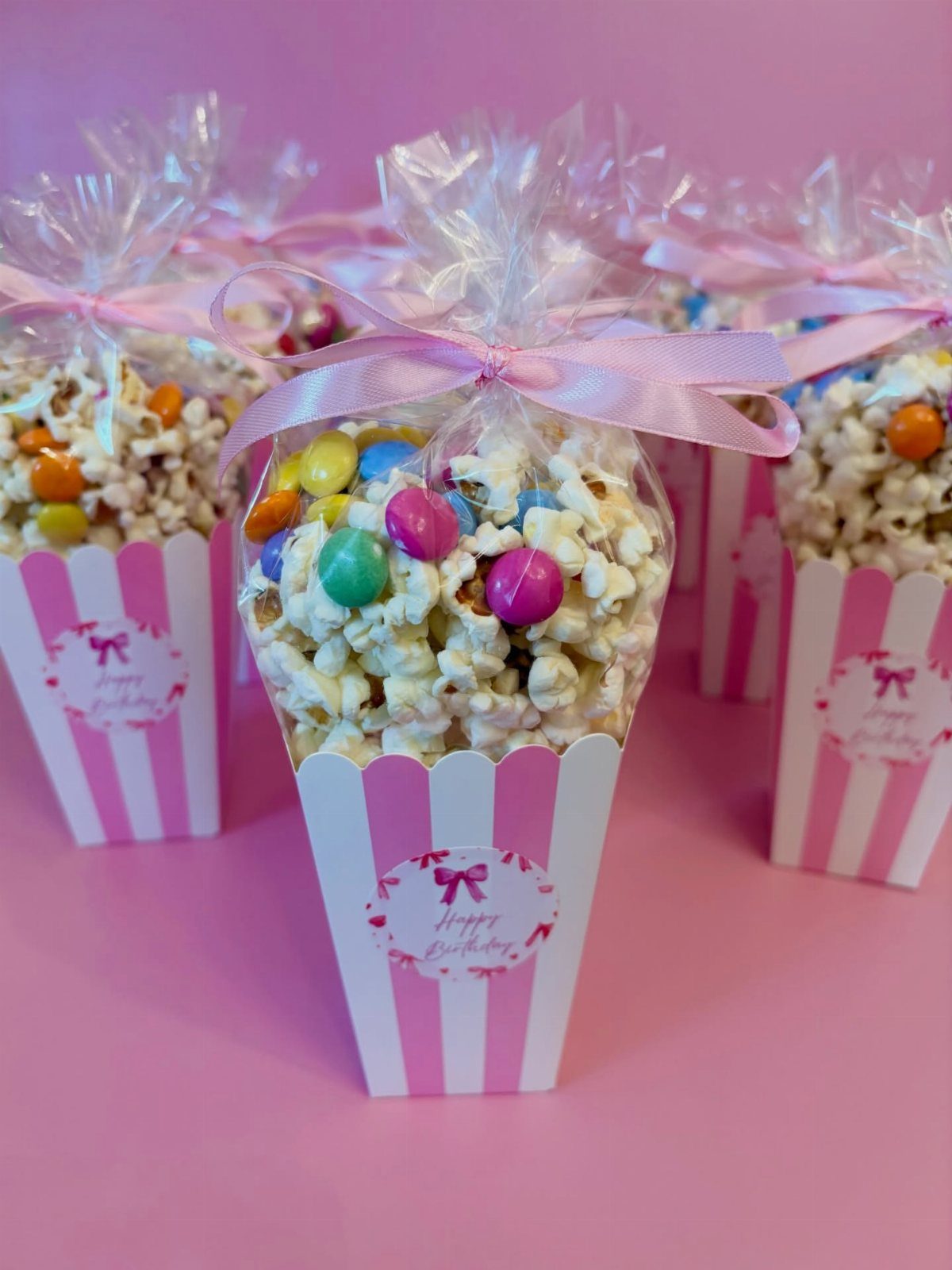 Pink and white striped popcorn cones filled with candy and tied with ribbons.