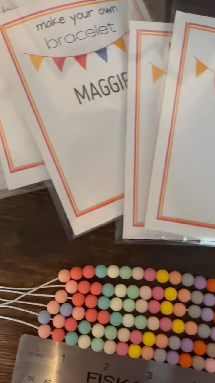 Pastel beads on strings and personalized bracelet making kits on a wooden table.