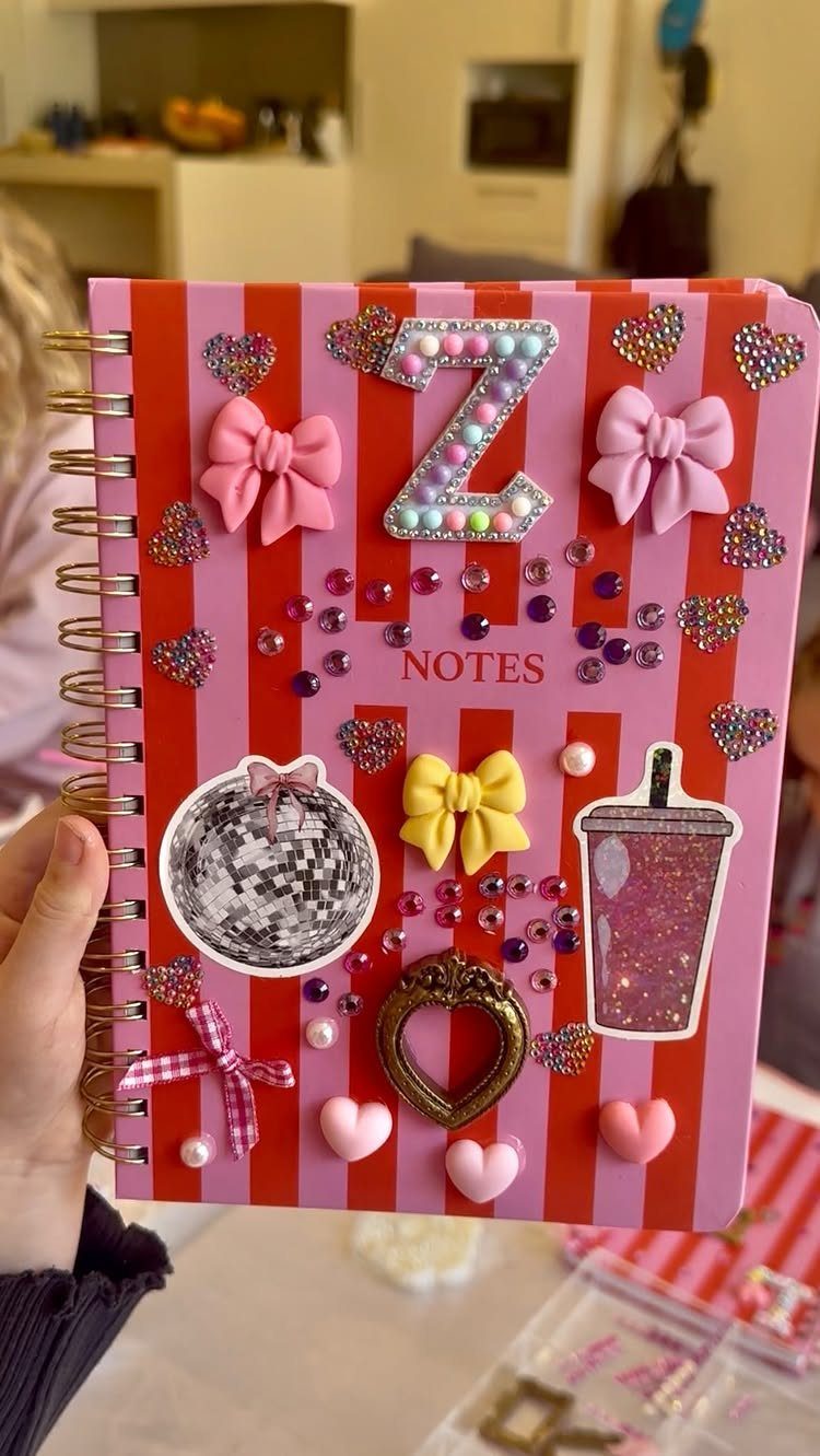 Decorated pink and red striped spiral notebook with jewels, bows, and stickers.