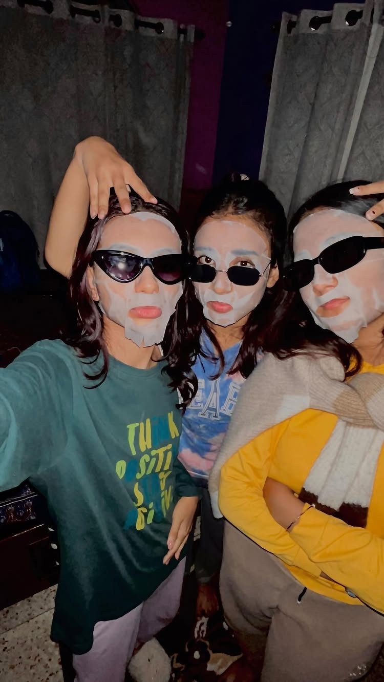 Three women wearing white face masks and sunglasses posing for a group selfie.