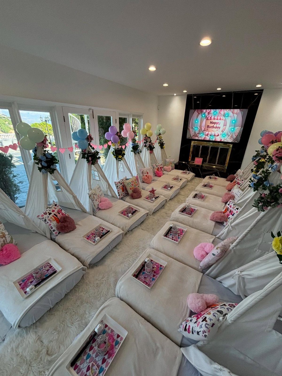 White teepee tents with pink pillows and trays arranged for a slumber party.
