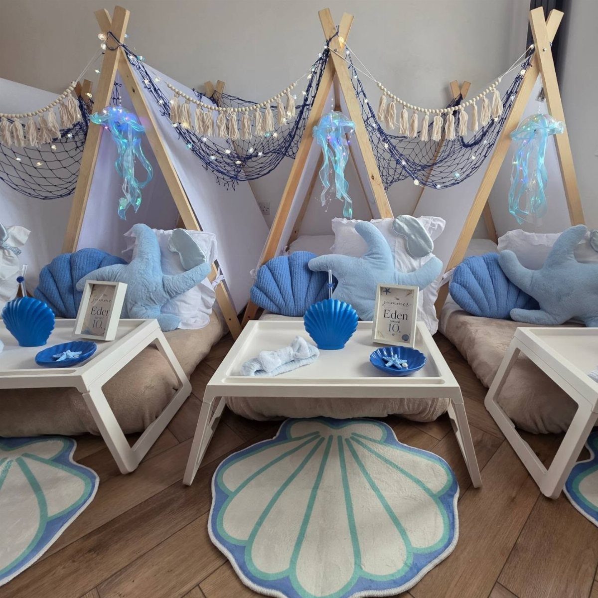 Three A-frame tents decorated with blue shells, starfish, and nets for a mermaid party.