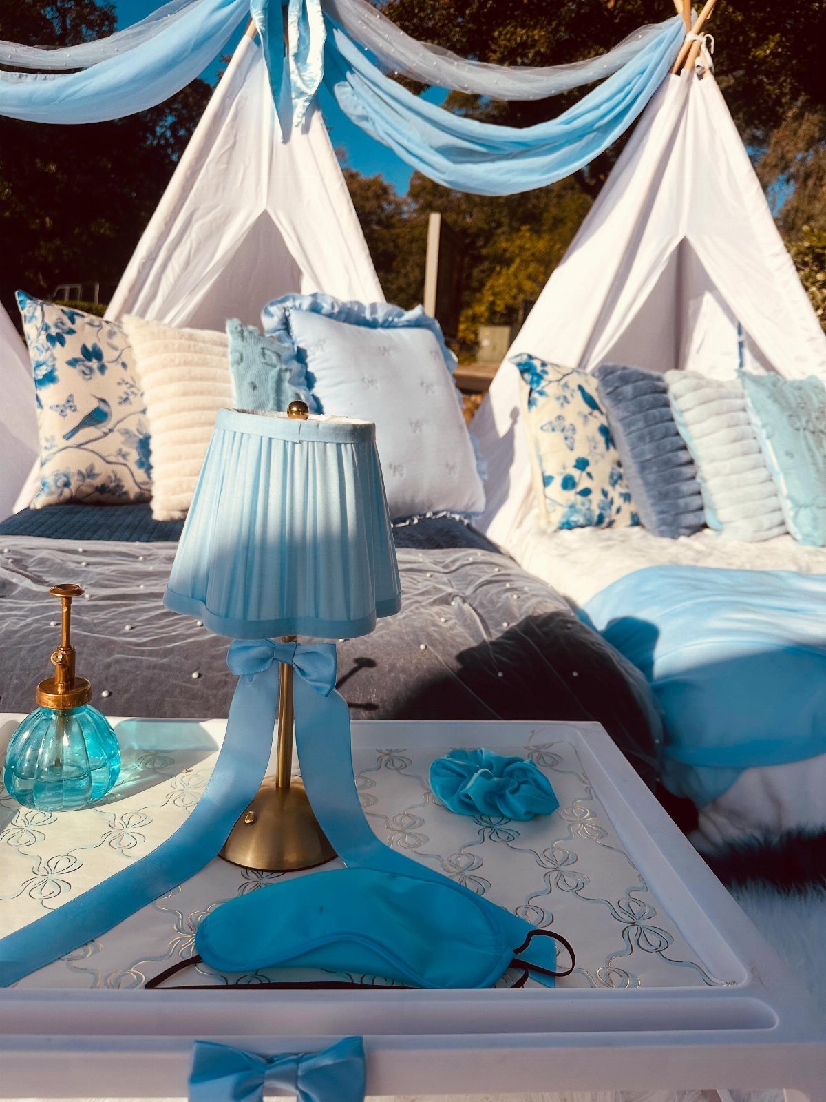 Two white teepee tents decorated with blue pillows and a matching blue lamp.