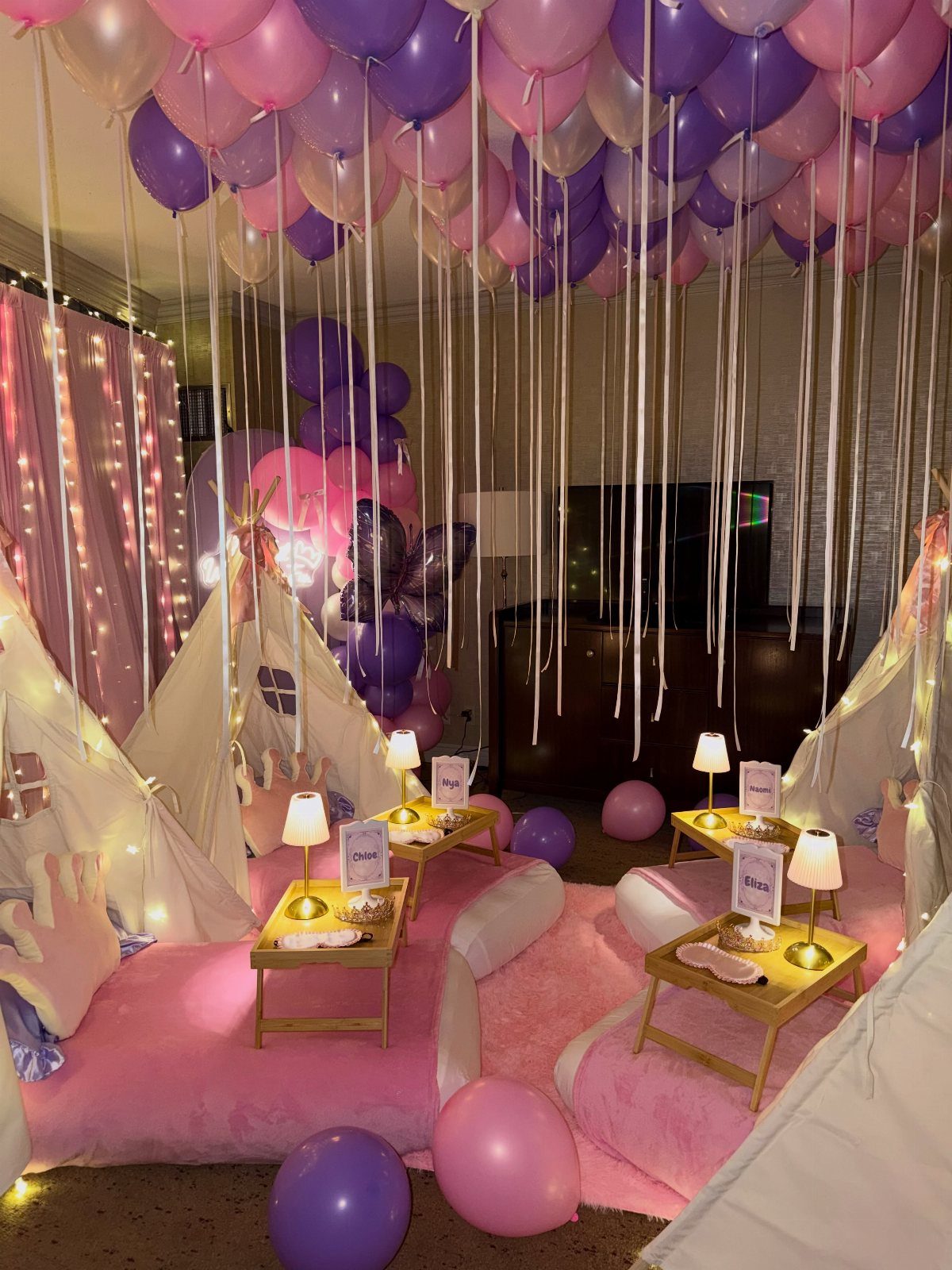 White teepee tents with pink bedding under a ceiling of pink and purple balloons.