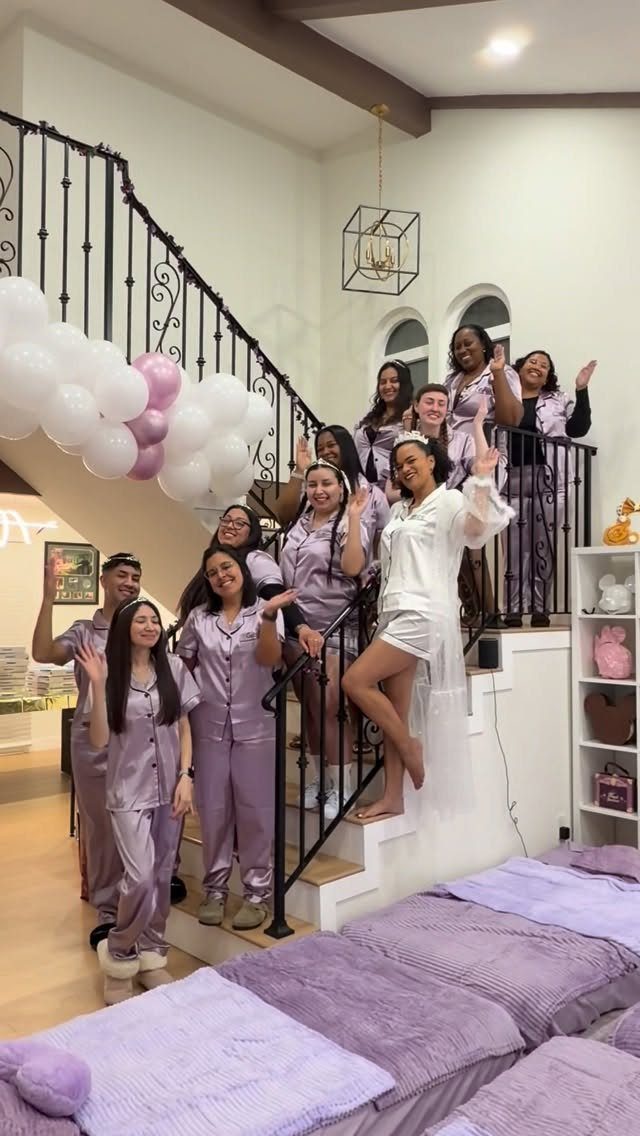 Group of friends in purple pajamas posing on stairs with purple balloons.
