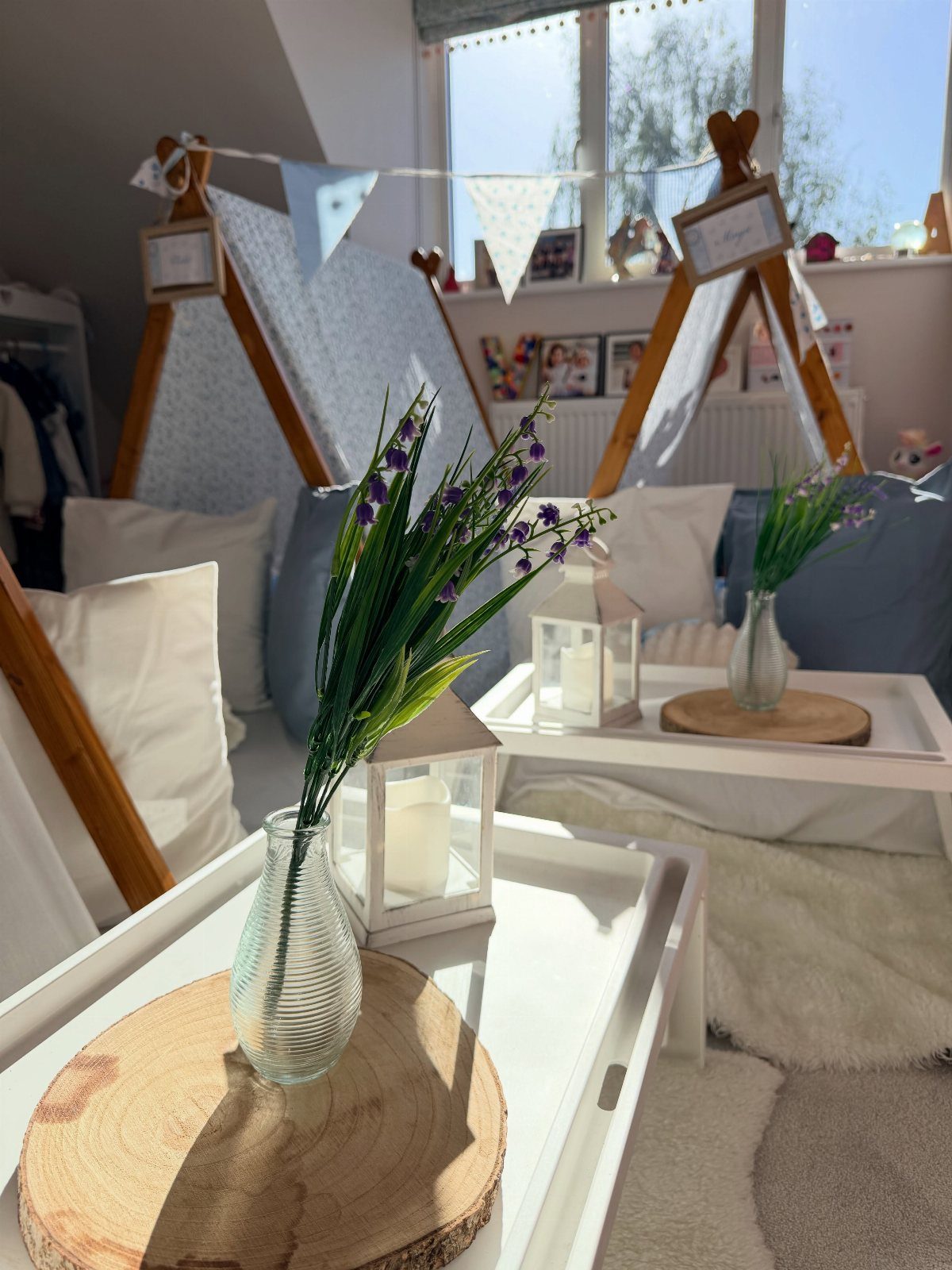 Wooden teepees and white trays with purple flowers and lanterns for a sleepover.