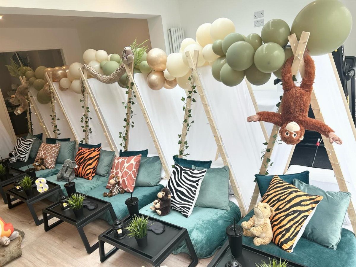 Safari themed sleepover setup with teepees, animal print pillows, and green balloons.
