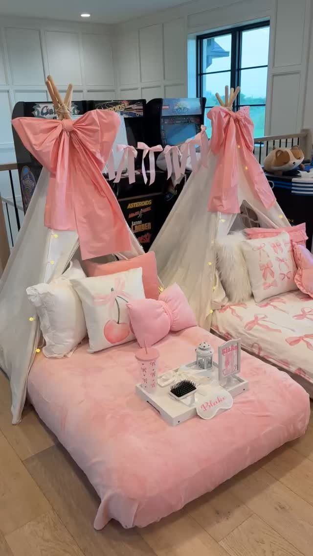 Two white teepee tents with pink bows and fairy lights for a slumber party.