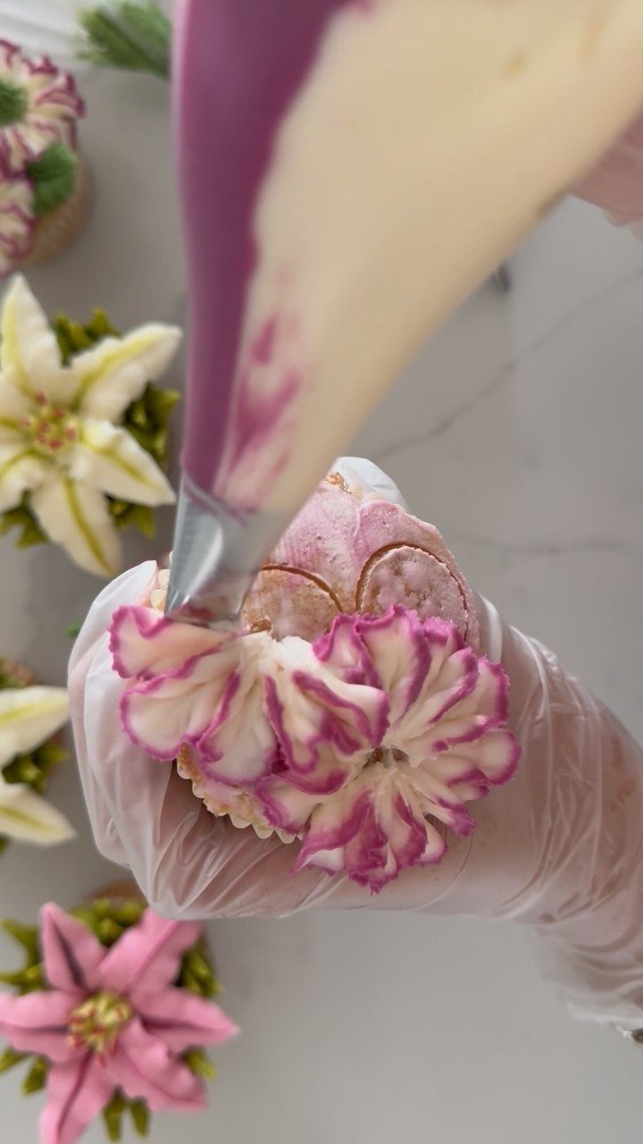 Hand piping pink and white swirled frosting onto a cupcake on marble surface