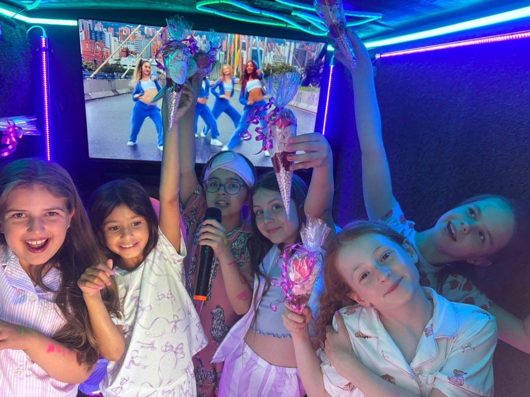 Five girls in pajamas posing with a microphone in a neon lit room.